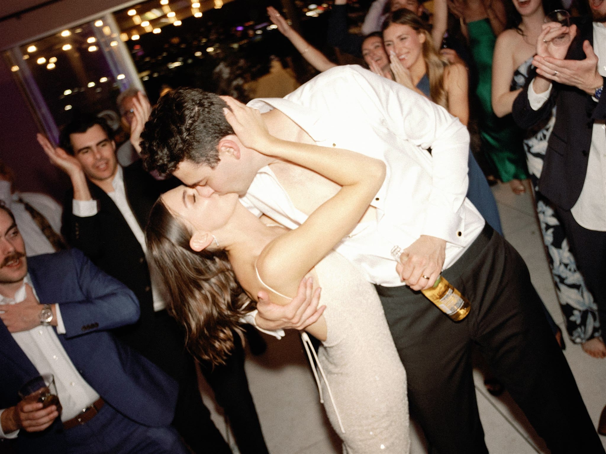 Bride and groom kissing on wedding dance floor with guests cheering