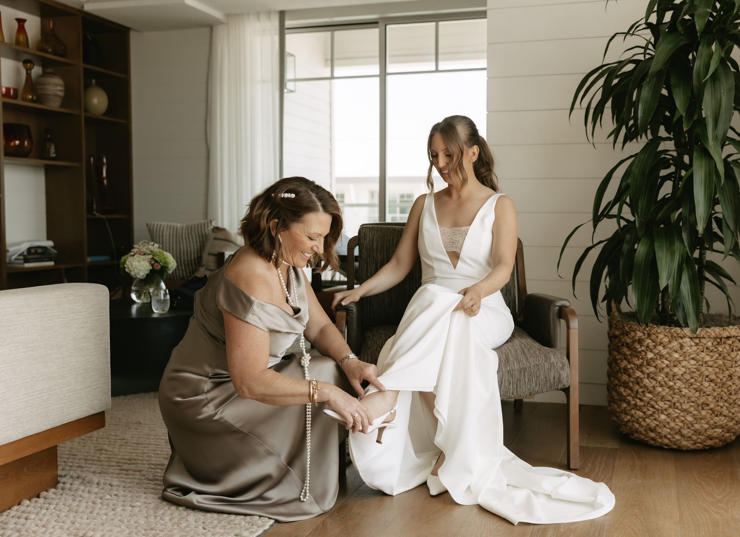 Mother of the bride helping bride put on shoes inside at The Seabird