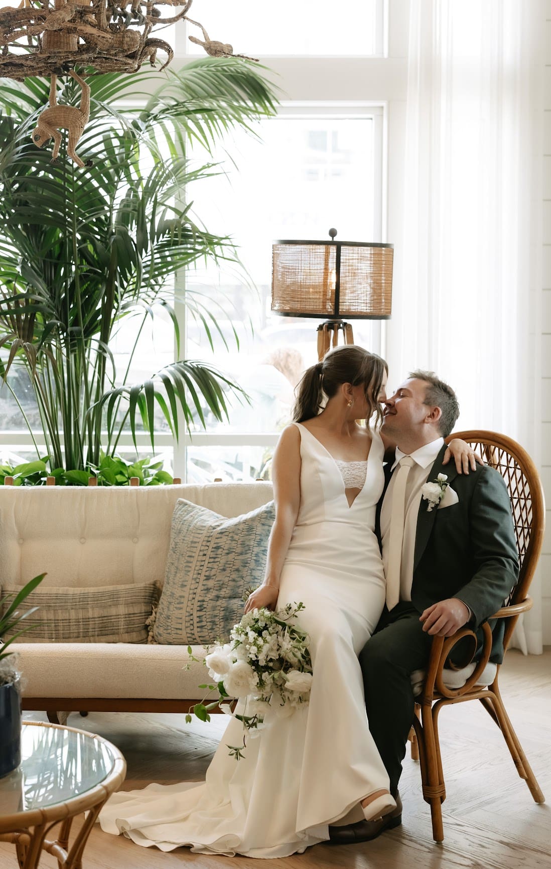 Bride sitting on groom's lap with a palm plant beside them at The Seabird